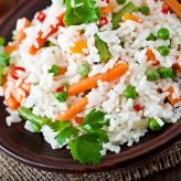 Appetizing healthy rice with vegetables in white plate on a wooden background.